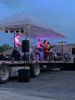 View from the audience of a band performing on stage. Five musicians can be seen with drums and guitars.