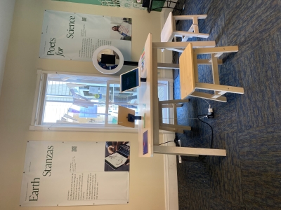 Office space with a wooden desk and bench. Literary posters hang on the wall beyond the desk, and there appears to be a tablet mounted for use on the desk.