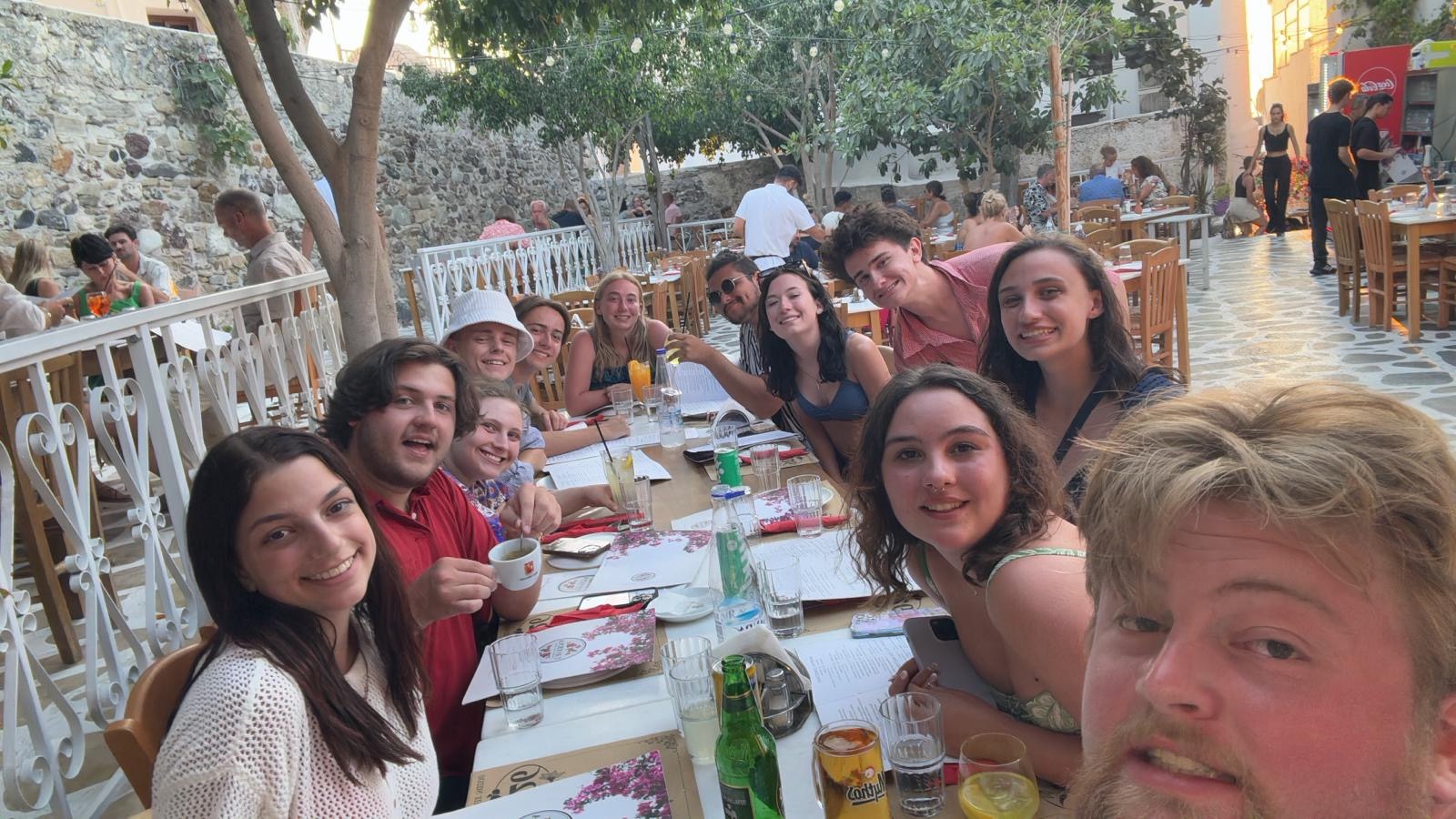 A group of students seated at a large table outdoors at a restaurant