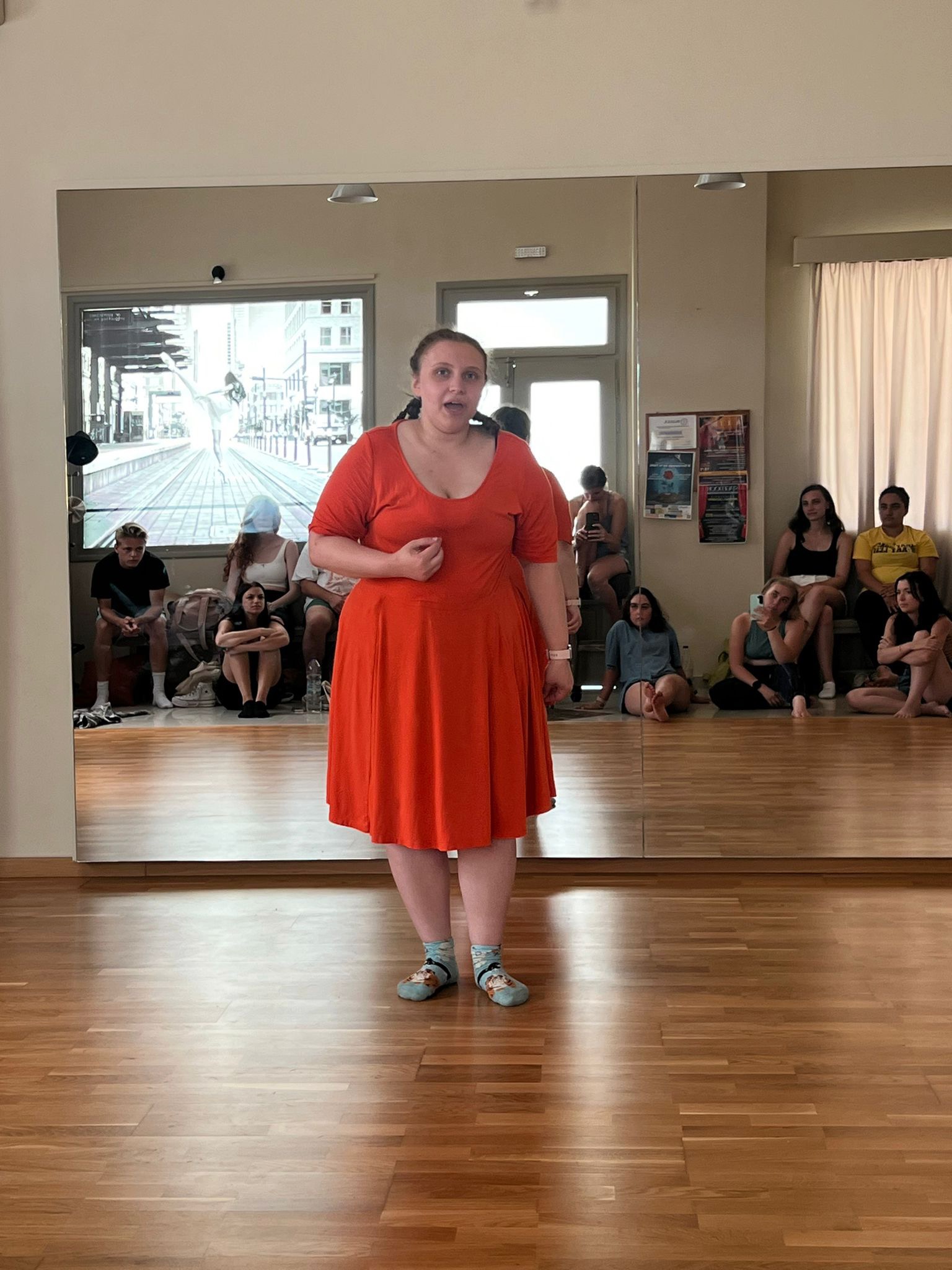 Bethie standing in front of a mirror showing a room full of seated students