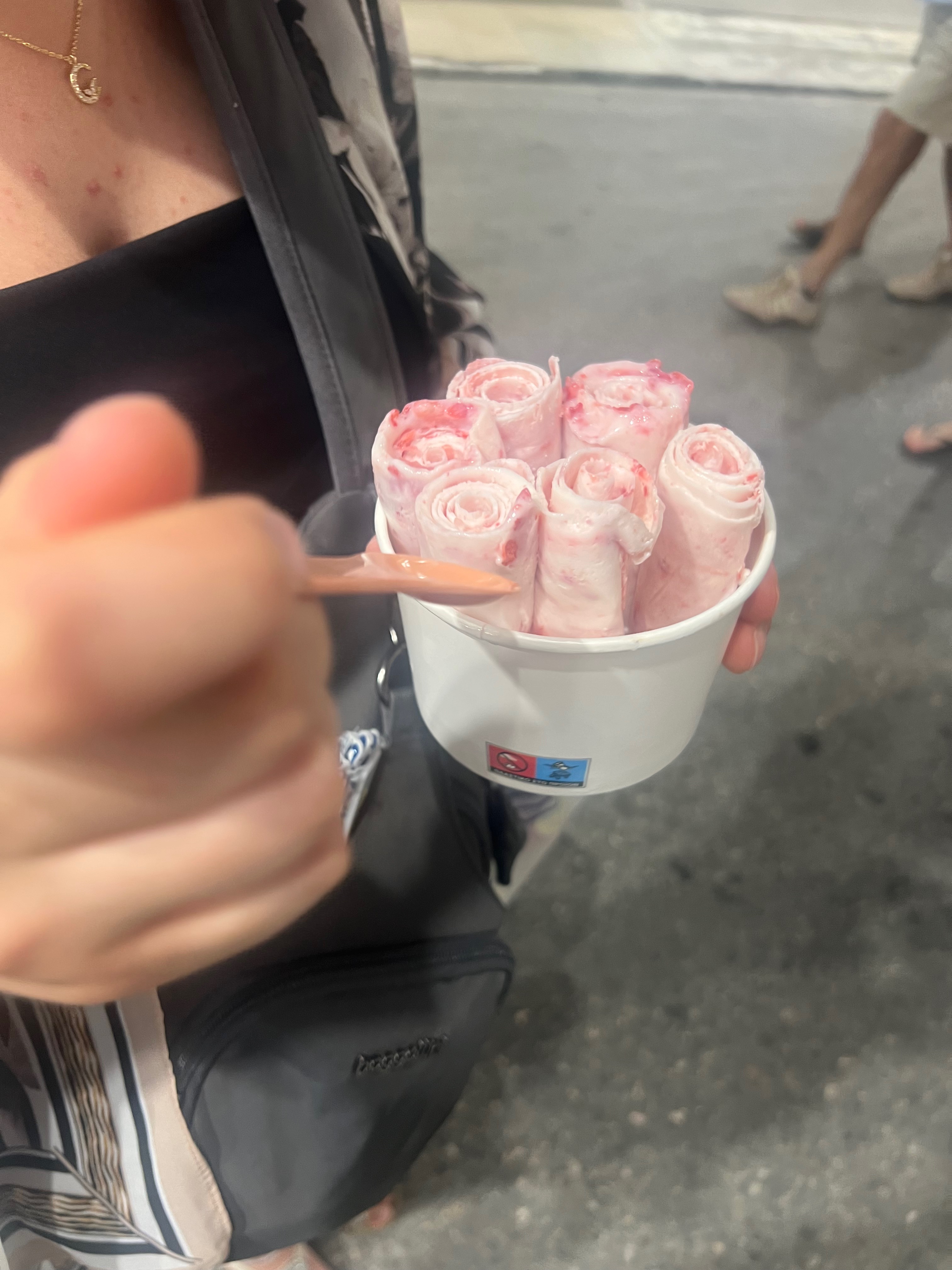 Someone holding pink rolled ice cream walking down the street