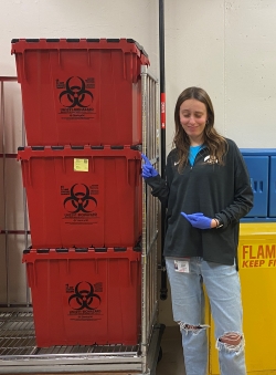 Cameron standing next to a stack of three red bins labeled for biohazardous materials