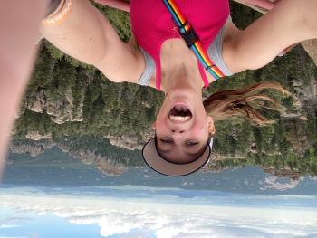 Selfie of Cameron on a hike, her mouth open in glee. She is wearing a sleeveless red-orange shirt.