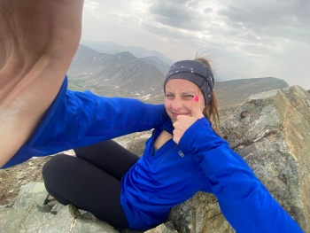 Selfie of Cameron seated on a rock and flashing a thumbs up sign to the camera. She's wearing a blue pullover sweater.