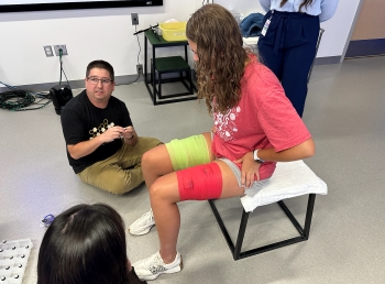 Ella seated with another person examining the sensors attached to her body