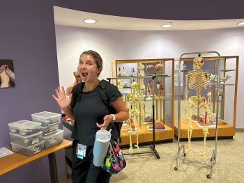 Ella poses with a jazz hand near a row of academic skeletons