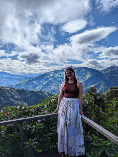 Emma posing in front of a gorgeous mountain view with beautiful blue skies with cumulous clouds, mountains, and purple flowers