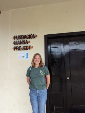 Emma posing in front of the Spanish language Manna Project stenciling on the wall