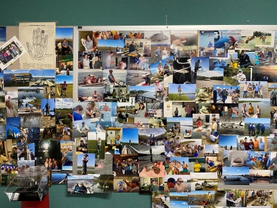 The image shows a bulletin board with hundreds of photos tacked on it. The photos are of all of the people who have worked at Baruch over the years and include several past Cornell Interns.