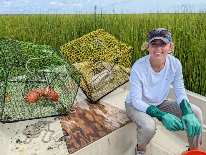 Emma sits in a boat with two mesh crate cages positioned behind and to her right.