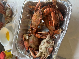 An aluminum cooking tub holds at least two whole crabs. Melted butter can be seen to the top and middle of the tub.