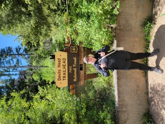 Jillian poses in front of a wooden sign that says "Devils Head Trailhead Pike National Forest."