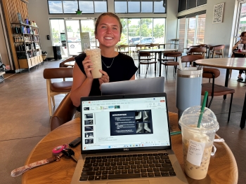 Photo Josalin has taken of her roommate Ella across the table in a coffee shop, Ella holding what looks to be a frappe or other frozen coffee drink.