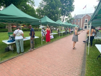 Dozens of green tents are sent up along a brick walkway. People are staffing each tent and others queuing to speak with them.