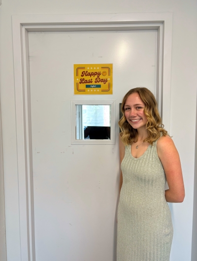 Kylie poses in front of a door with a special placard that says "Happy Last Day"