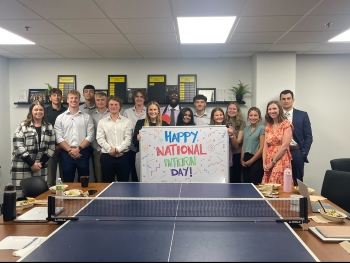 Interns gathered around a ping pong table with a big National Intern Day sign