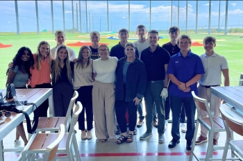 Group shot of the interns at Pinseekers, the concourse where golf balls soar visible in the background