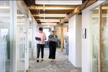 Krystin and another intern stroll down the hallway of an office.