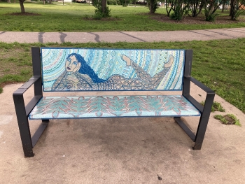 Bench at Mayo Memorial Park. A mural drawn on the bench shows a woman reclining on her stomach with her hands clasping her cheeks in a state of wonder.