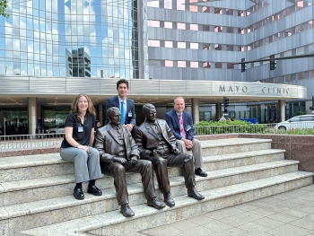 Moodi, Laura, and Dr. St. Louis sit on the steps with the statues of the Mayo brothers outside the Mayo Clinic.