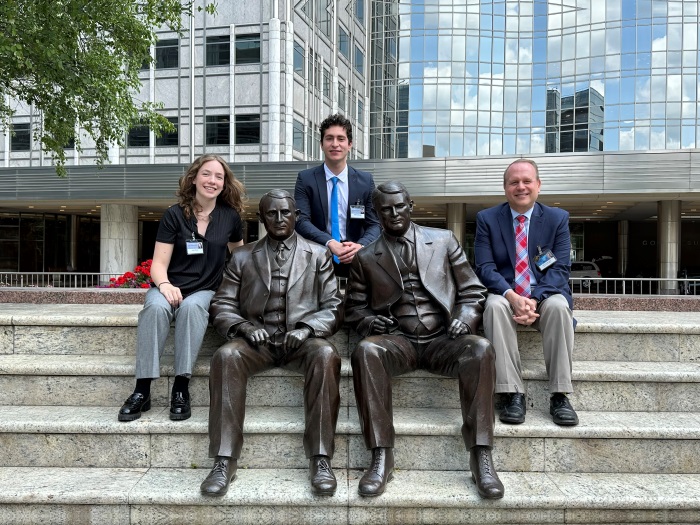 Moodi, Laura, and Dr. St. Louis sitting together on the steps with the Mayo Brothers statues in front of Mayo Clinic