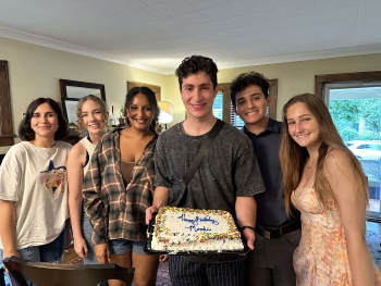 Group photo of Moodi's fellow interns surrounding him as he holds up his birthday cake