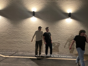 Three college-aged men idle in a lit parking lot area.