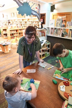 Nellie helps two children seated at a table with their craft activities