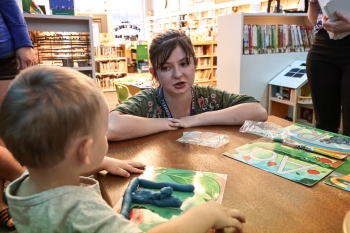 Nellie crouches next to a table, speaking to a young child with enthusiasm.