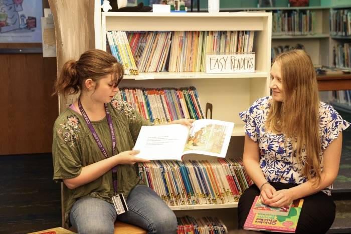 Nellie reads a story to children with a librarian to her left