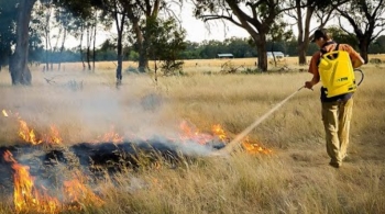 Firefighter walking along grassland area spraying water