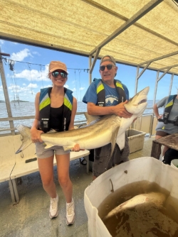 Anna and an older man each hold one end of a medium-sized shark. Anna is on the tail end, the man on the head end.