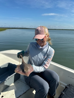 Anna smiles while holding a small manta ray. She is in a boat.