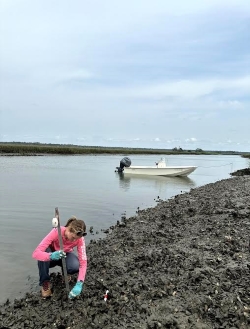 Shot farther back of Anna digging along the bank of a waterway
