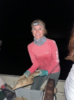 Anna smiles on a boat at night. She is holding an aquatic creature, perhaps a stingray or long-nose gar
