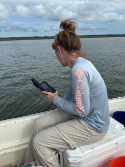 Anna sits on a cooler at the side of a boat looking out into the water.