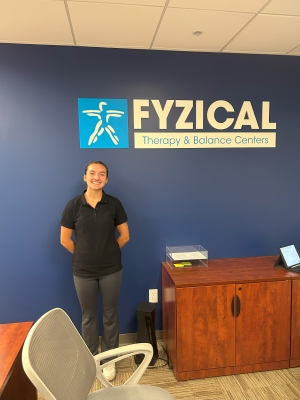 Alyza posing by the indoor sign for Fyzical Therapy and Balance Centers