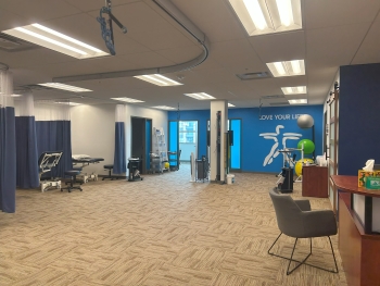 Physical therapy office area: open flooring in the middle with little cubicles and patient stations around the walls surrounding