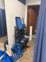 Weights, rubber bands, and other rehab equipment are organized in a black racking area along a wall.