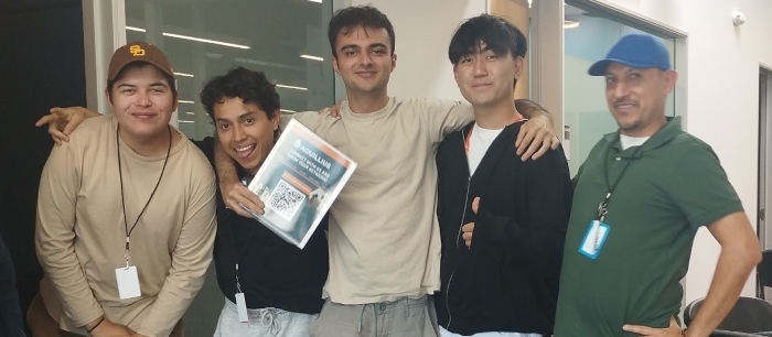 Group photo of Aras (center) and four other colleagues in a break room area, their arms around each other, standing and facing the camera