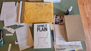 View looking down at a table with various papers, a book, and other parts of a packet to mail out to subscribers
