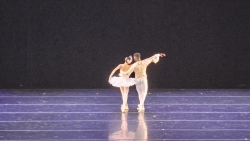 Two ballet dancers on a stage, engaged in their craft and dressed in light colors of pink and white for their performance