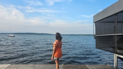 Claudia stands with her back to the camera on a dock, looking out at the vast Chautauqua Lake