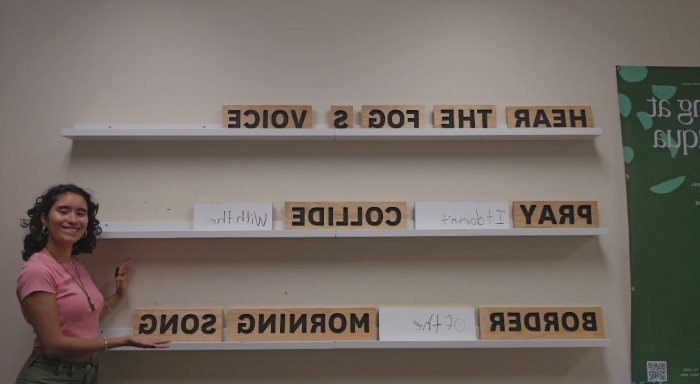 Claudia poses next to a large tiled board with printed word blocks inserted into the runners. The words appear backwards because of the camera