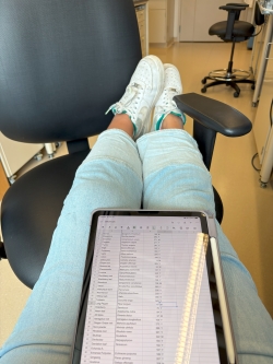 View of legs propped up on a chair, a electronic tablet sitting in the lap and displaying a list of botanicals