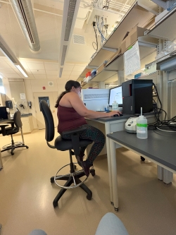 View from right right side of a woman sitting at a computer desk actively working and interacting with what is on the screen