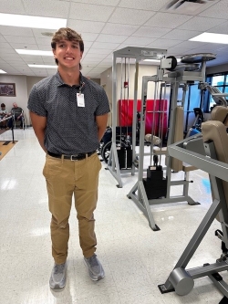 Charlie poses in the physical therapy room with exercise equipment in the background