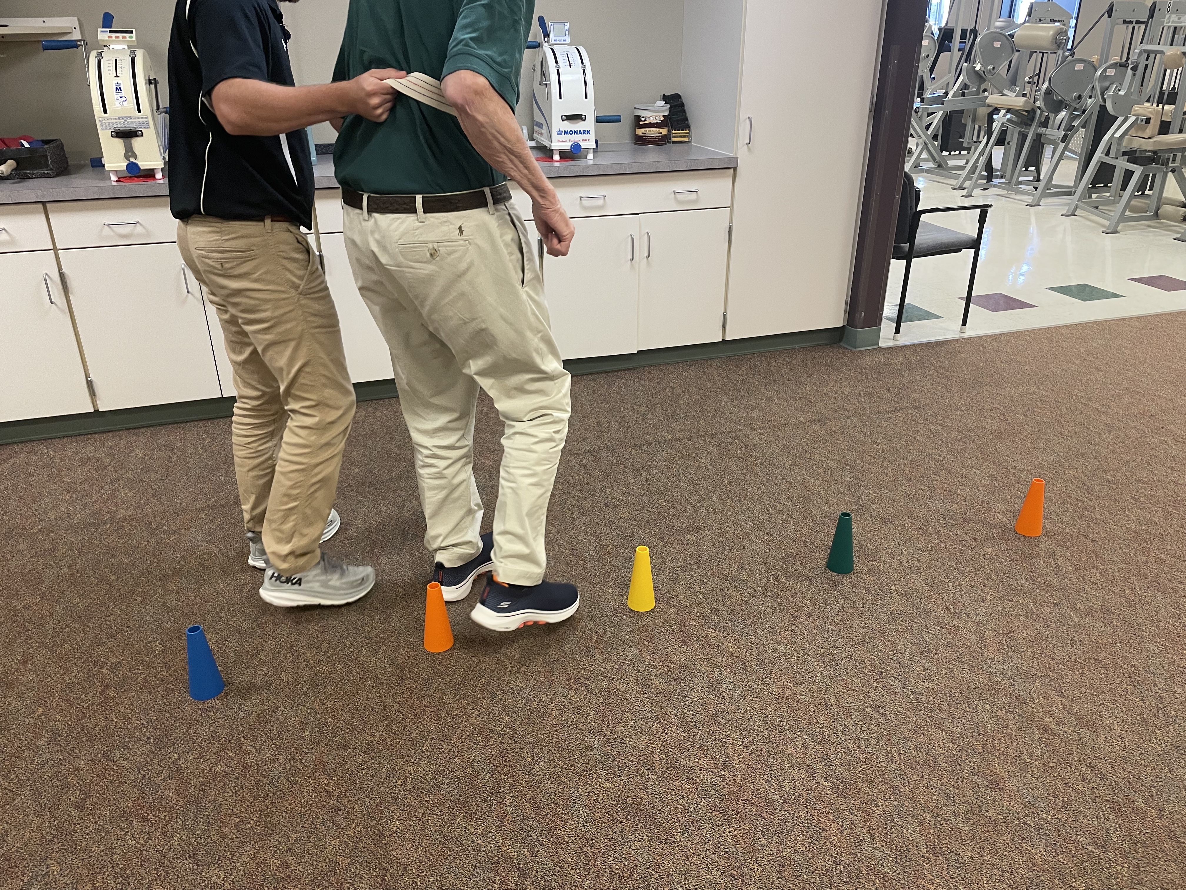 Charlie heling a patient through an exercise involving cones on the floor