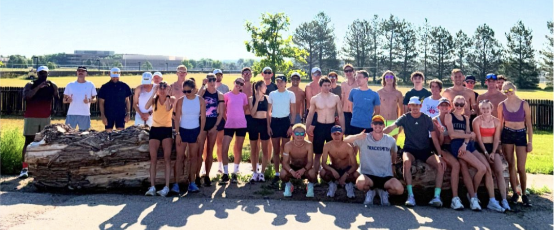 Group photo of about two dozen runners posing near a fallen tree stump