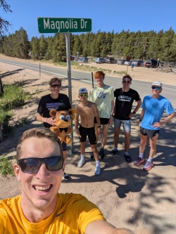 Selfie of Isaac with a group of five other young men in the background, all dressed for summer running